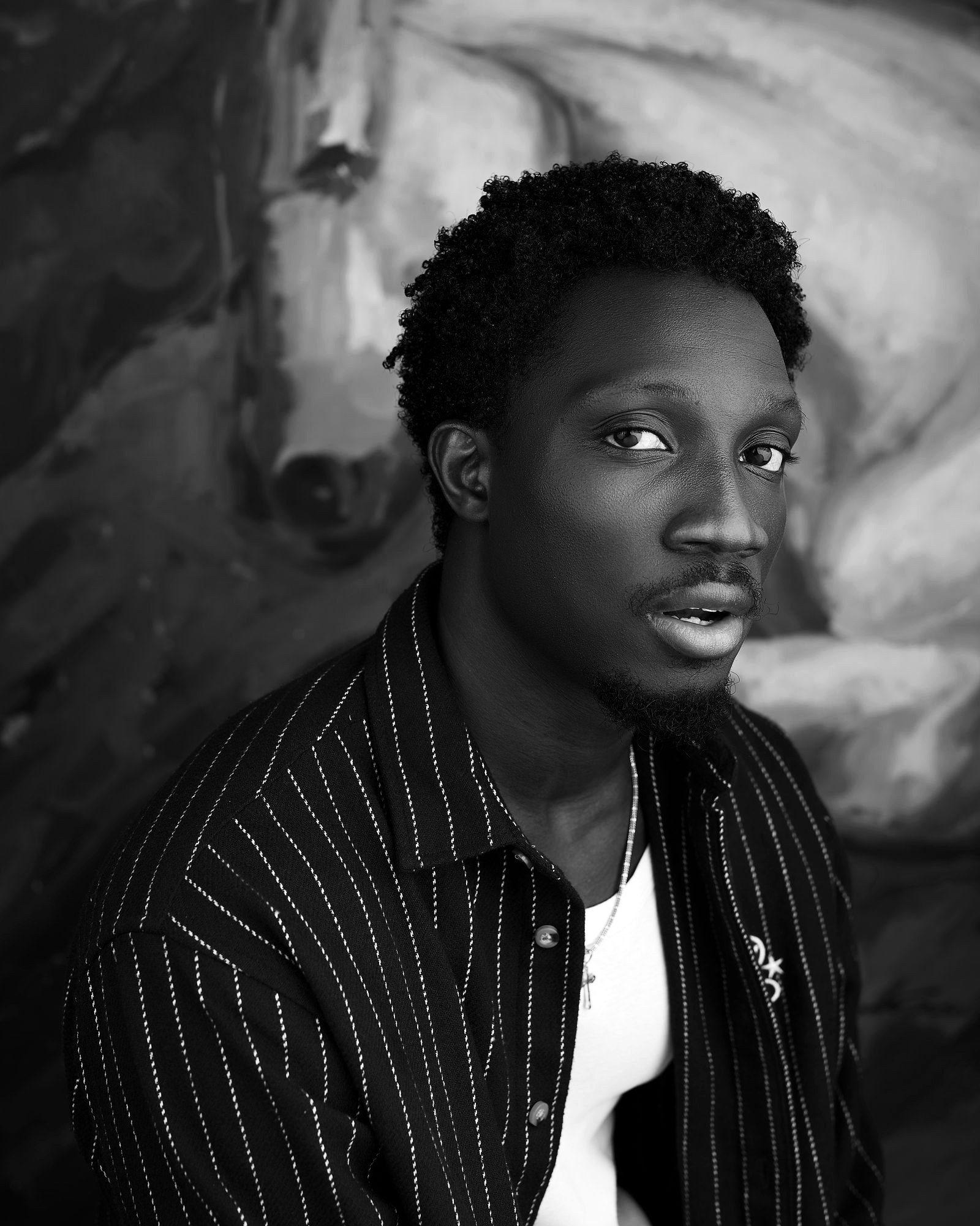 Greatman Takit in a striped shirt against a painted studio backdrop.
