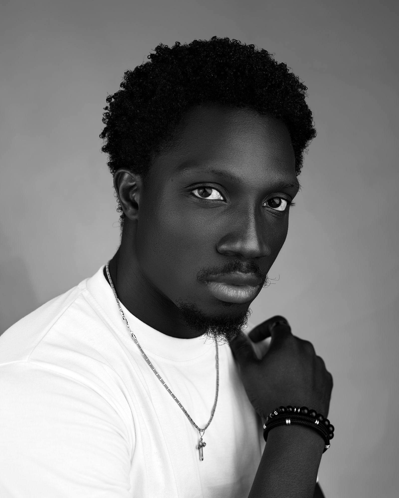 Close portrait of Greatman Takit looking directly at the camera, a cross pendant at his neck.